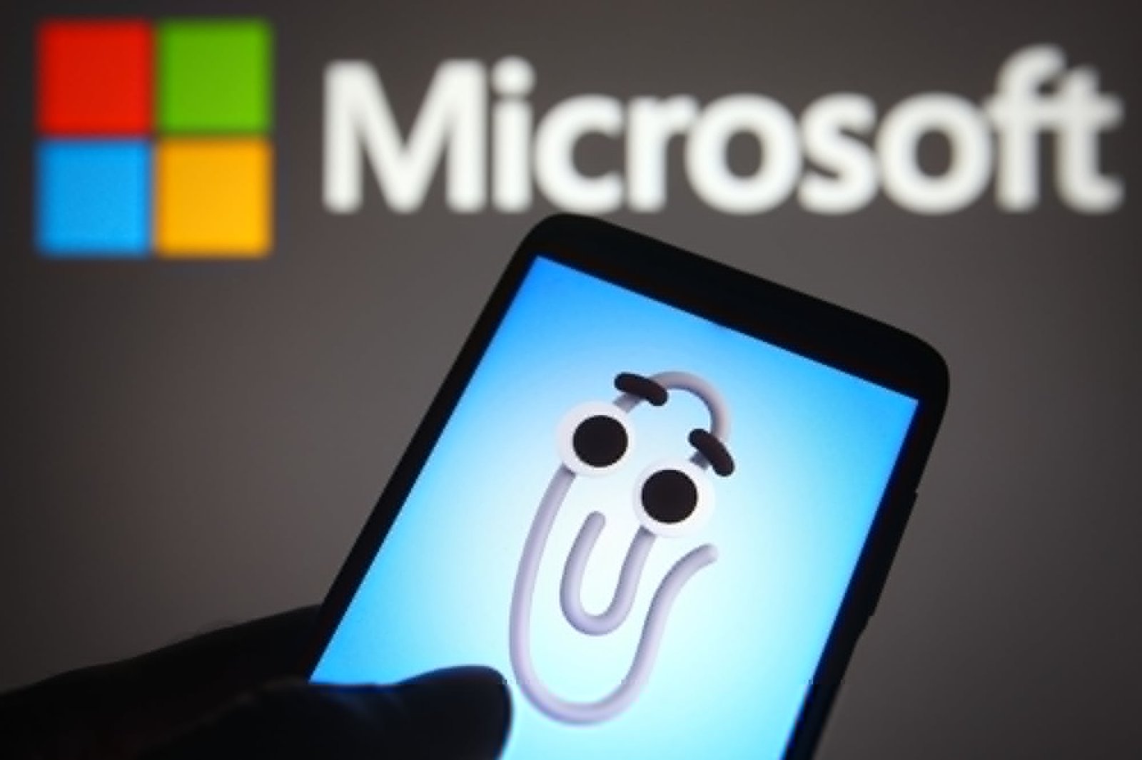 An animated virtual assistant Clippy (Clippit) is seen displayed on a smartphone screen and Microsoft logo in the background.